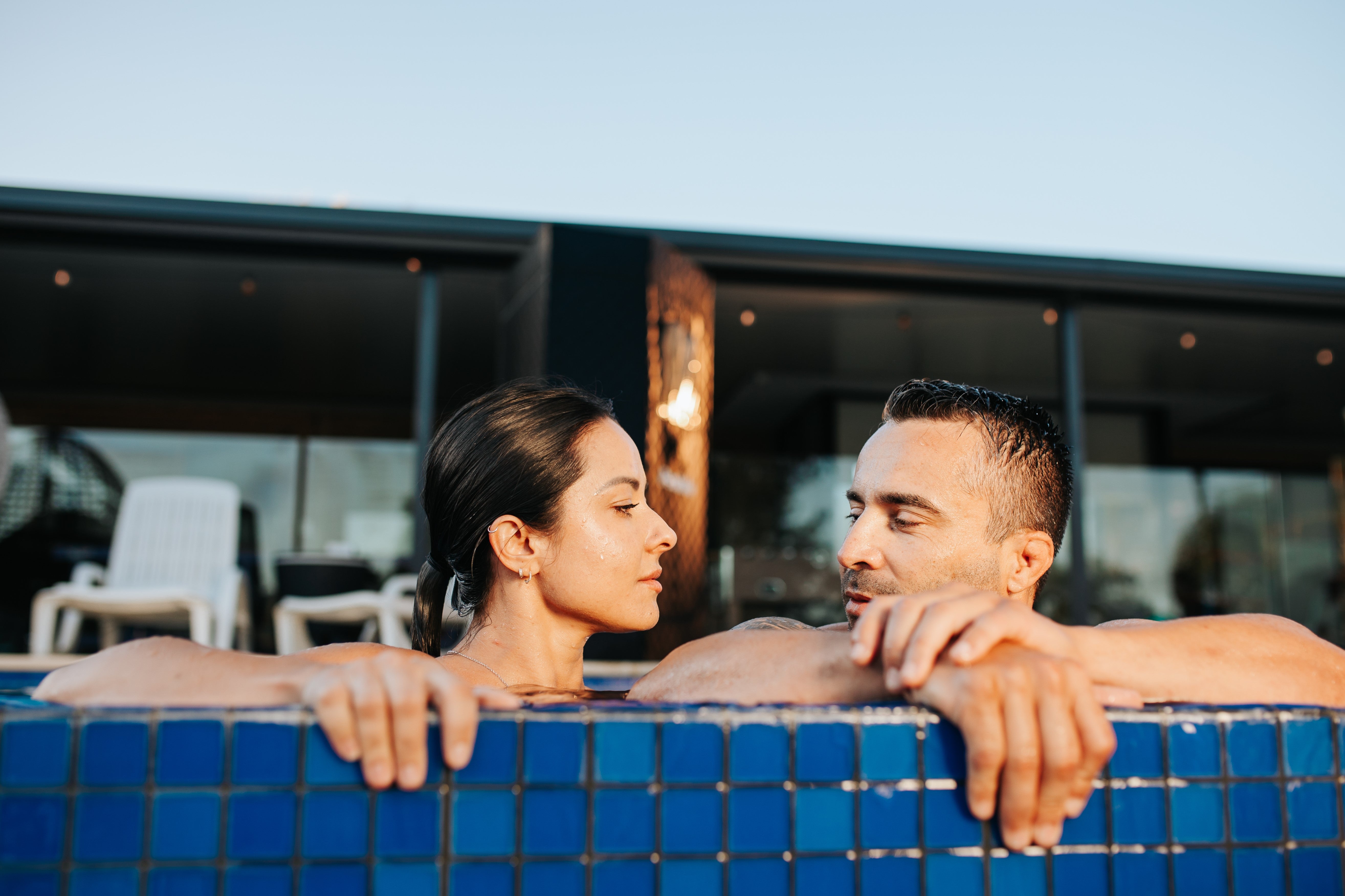 Couple sharing a serene and connected wellness moment in the crystalline waters of a pool, with the elegant PeakMe steam sauna in the soft-focused backdrop, symbolizing the ultimate at-home luxury retreat experience.