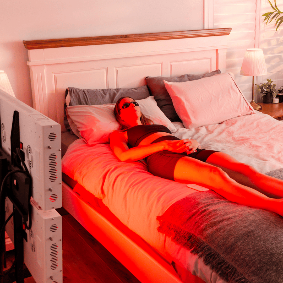 Woman lying on bed with protective goggles, immersed in red light therapy using PeakMe's advanced equipment for enhanced wellbeing and recovery.