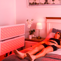 Woman reclining comfortably in bed, engaging in a red light therapy session with 2x PeakMe Pro 1500 panels, enveloped in a warm, soothing glow that promotes relaxation and skin health in a cosy home setting.