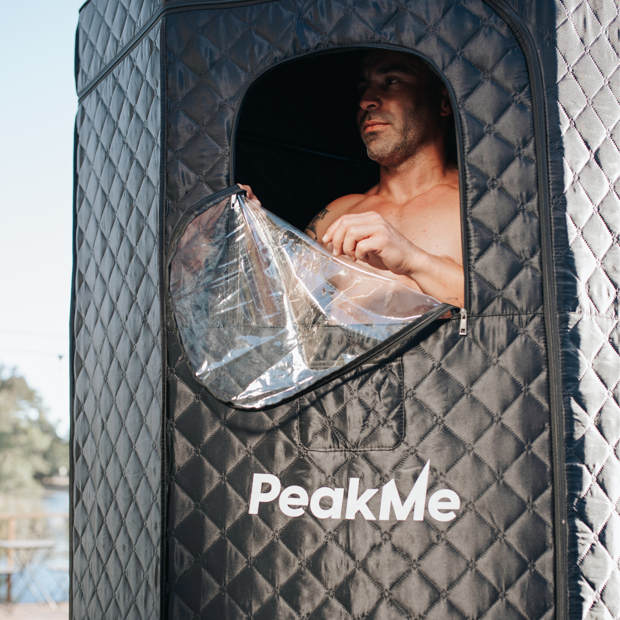 Man peering out from a PeakMe sauna tent, engaged in a personal heat therapy session, enhancing wellness with a home sauna experience.