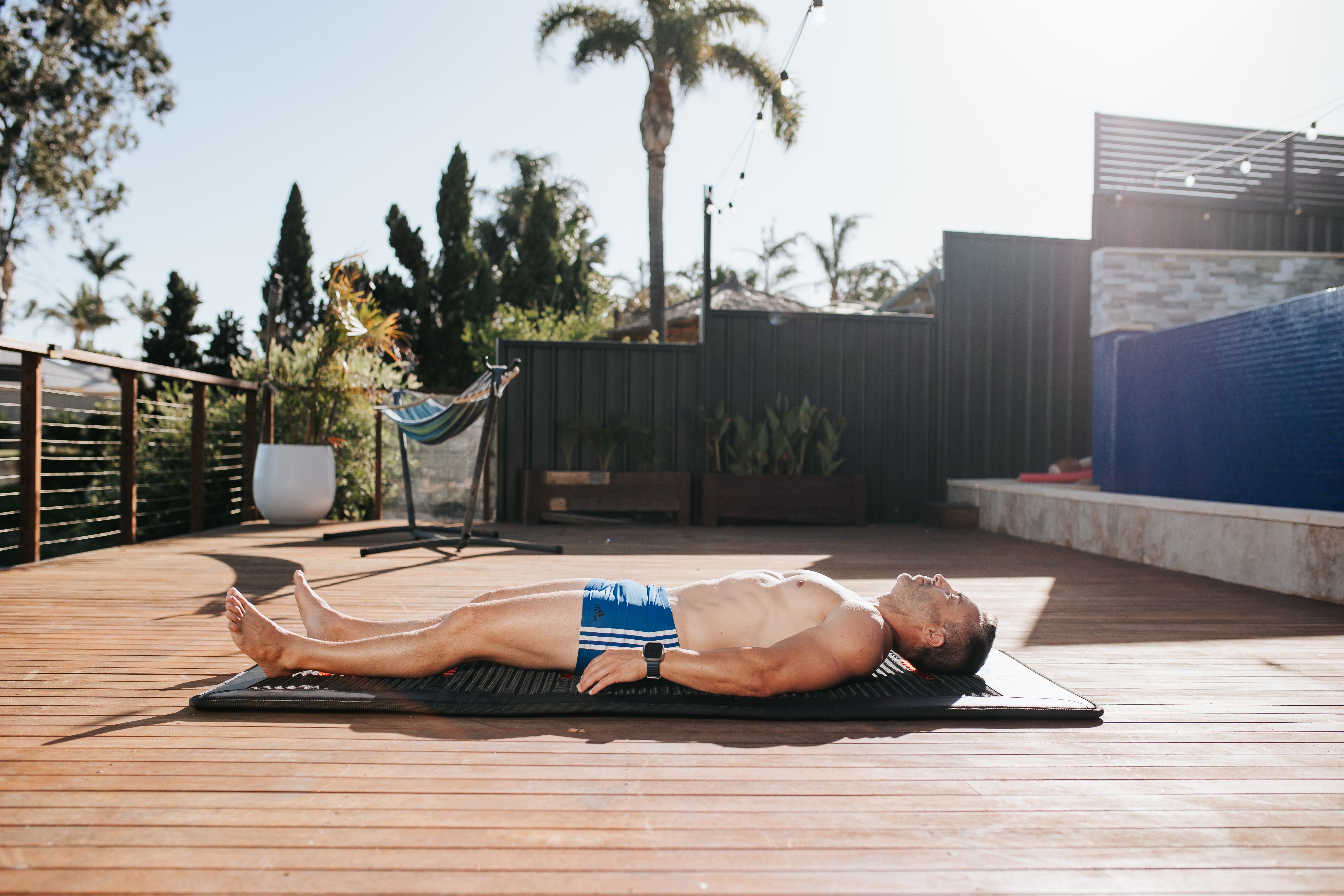 Man absorbing the sun's warmth while lying on a PeakMe PEMF mat in a tranquil backyard setting, a personal wellness retreat fostering relaxation and health.